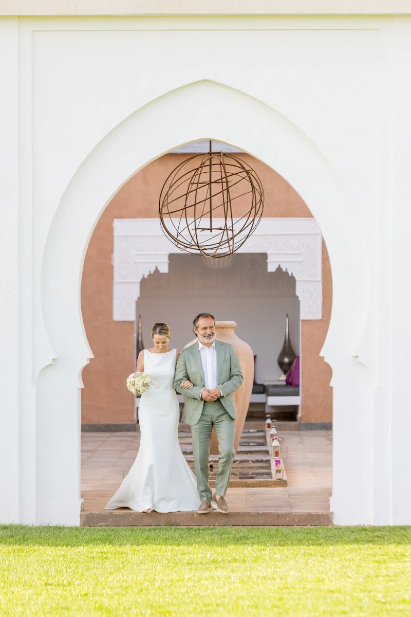 Mariée accompagnée sous une arche marocaine avant sa cérémonie à MarrakechBride walking with her escort beneath a Moroccan arch before her ceremony in Marrakech