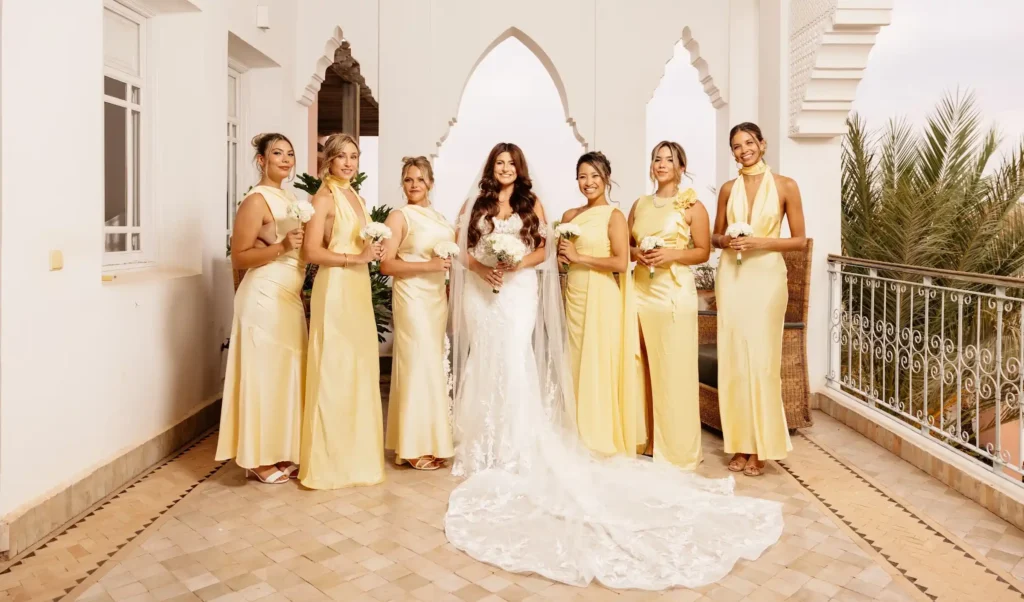 Mariée en robe de dentelle blanche entourée de six demoiselles d’honneur en robes jaune pâle sur une terrasse à Marrakech.Bride in a white lace gown with six bridesmaids in pale yellow dresses on a terrace in Marrakech.