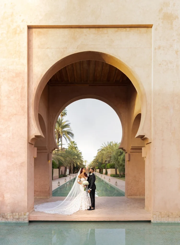 Mariés posant sous une grande arche marocaine devant un bassin à MarrakechNewlyweds posing beneath a large Moroccan arch beside a pool in Marrakech