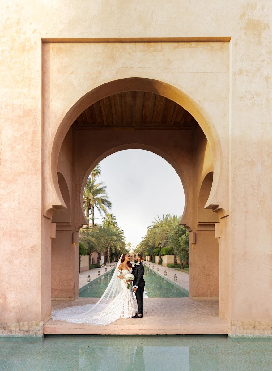 Mariés posant sous une grande arche marocaine devant un bassin à MarrakechNewlyweds posing beneath a large Moroccan arch beside a pool in Marrakech