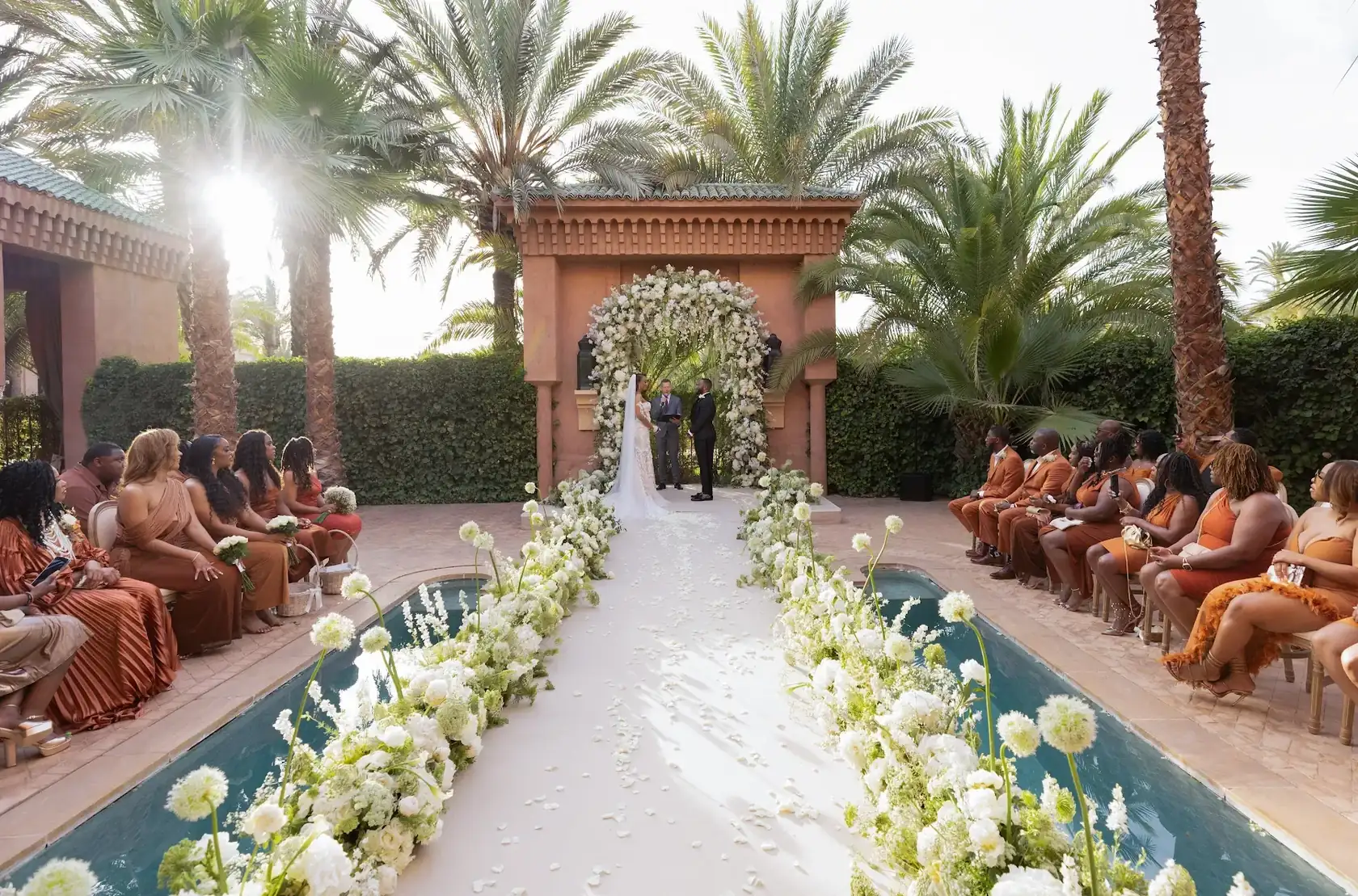 Mariés sous une arche de fleurs blanches lors d’une cérémonie au bord d’une piscine à MarrakechCouple beneath a white floral arch during a poolside wedding ceremony in Marrakech