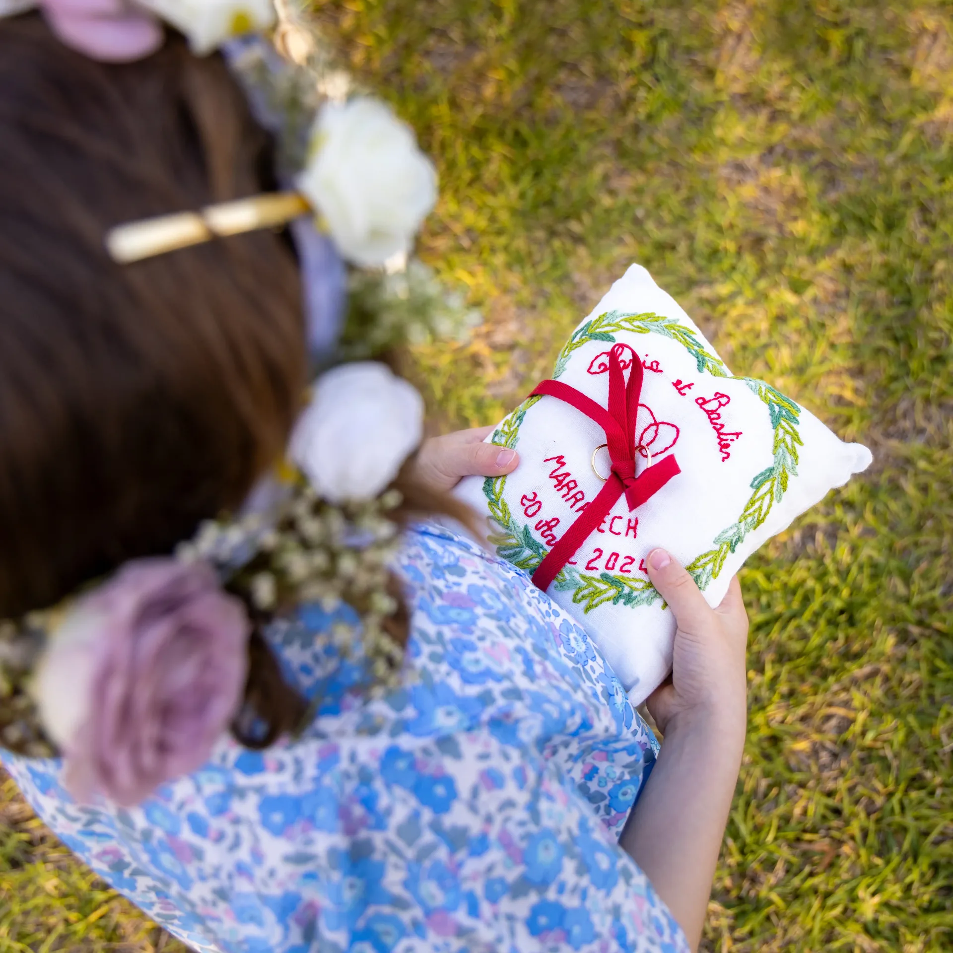 nfant tenant un coussin d’alliances brodé et personnalisé avec un ruban rougeChild holding an embroidered personalized ring pillow with a red ribbon